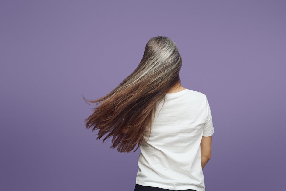 Rear view of a woman with long, flowing gray hair against a purple backdrop.