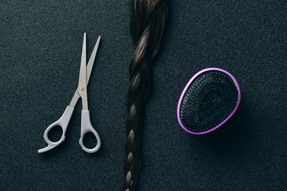 Close-up of hairdressing scissors, braided hair, and brush on black background.