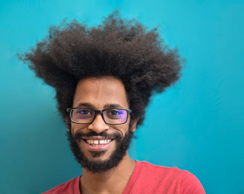 Vibrant portrait of a smiling man with afro hair and glasses against a teal background.