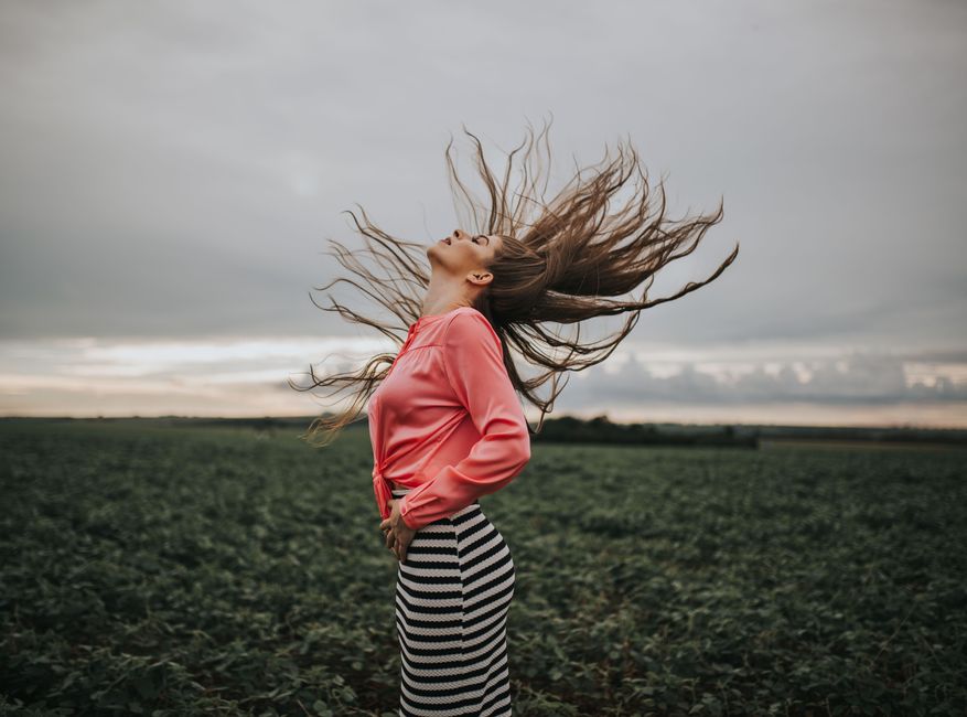 Captivating image of a woman in a field enjoying the wind with hair blowing freely, exuding freedom and style.