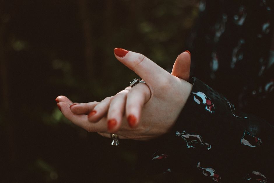 Artistic close-up of hands adorned with stylish rings and red nails, emphasizing elegance.
