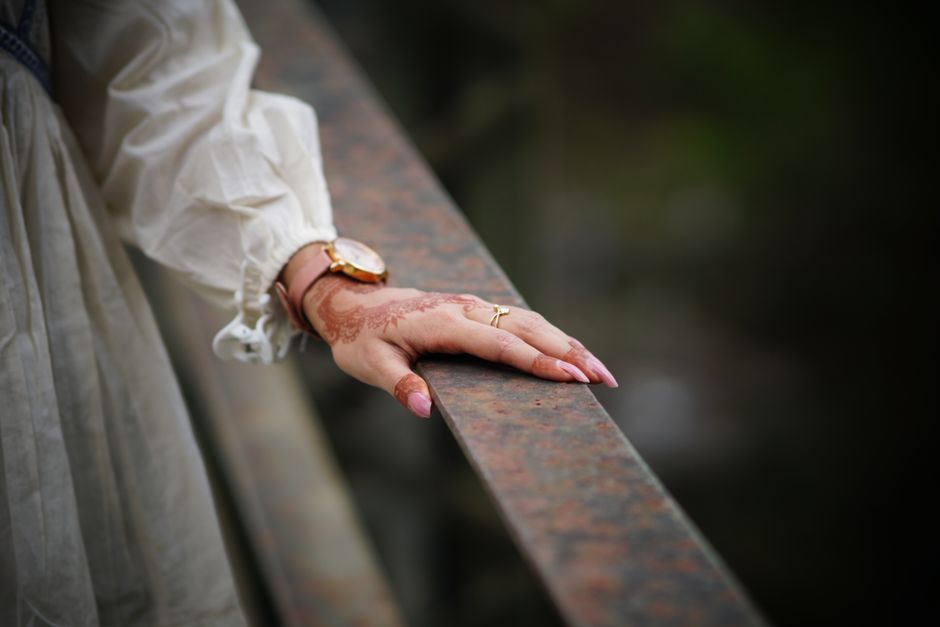 Close-up of a woman's hand with henna, wearing a watch and rings, resting on a railing.