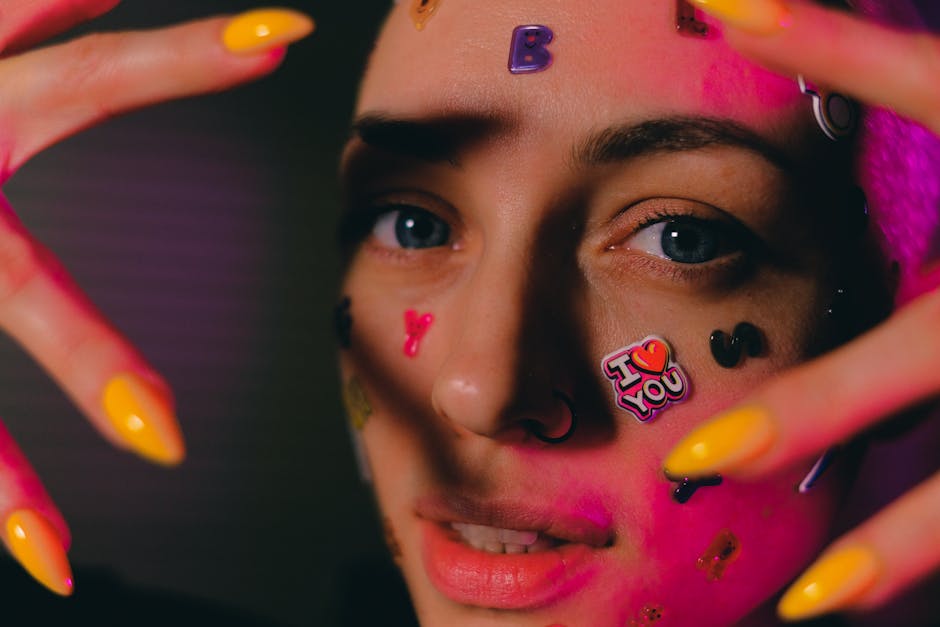Crop young bald female with multicolored stickers on face raising hands near face and looking at camera in dark studio