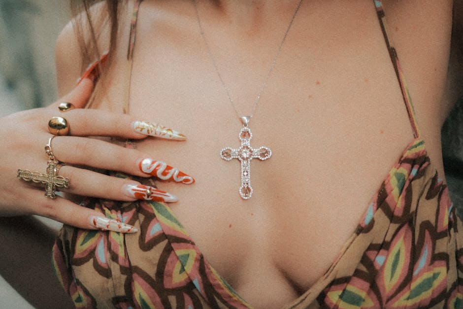 Close-up of a woman wearing a cross necklace with artistic nails, showcasing bohemian style.