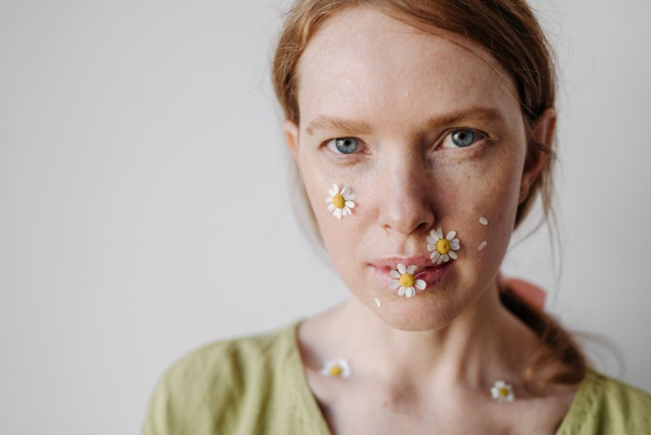 Close-up portrait of a woman with daisies on her face in a studio setting.