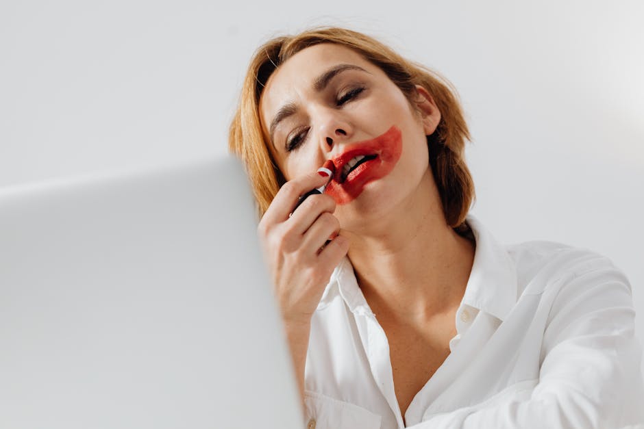Young woman playfully applying red lipstick, creating an artistic makeup effect.