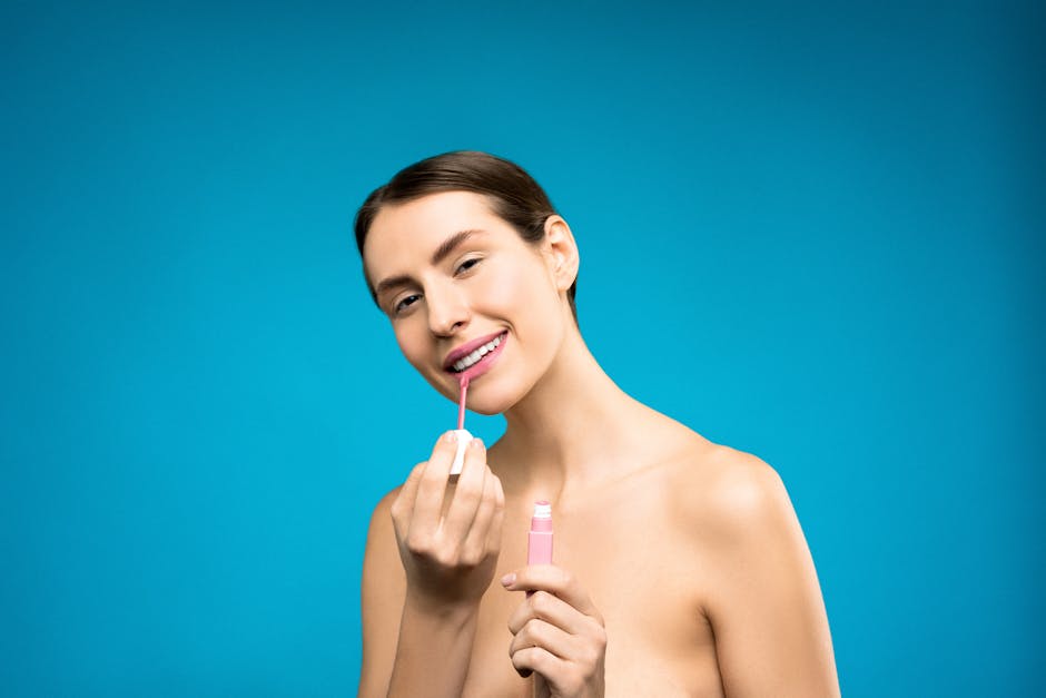 A smiling woman applies pink lipstick against a vibrant blue background, showcasing beauty and confidence.