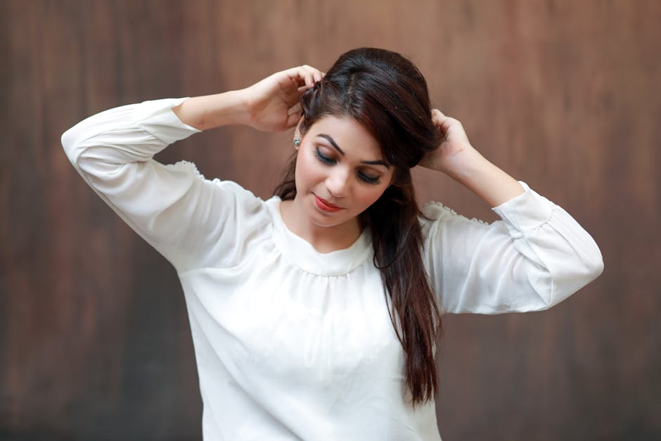 Portrait of a woman in a white blouse adjusting her hair against a brown background.